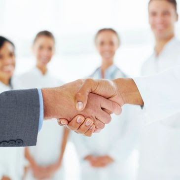 An administrator shaking hands with a doctor as the rest of the team looks on